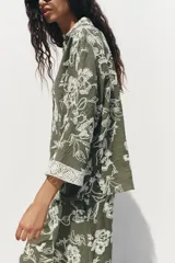 Camisa verde militar con bordado floral blanco, cuello solapa, escote en pico, manga tres cuartos con detalle de guipur y cierre frontal con botones.