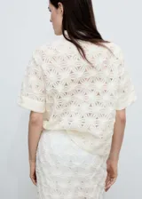 Blusa color crema con textura calada y flores en relieve, cuello camisero, manga corta y cierre de botones en el cuello.