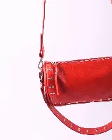 Bandolera marrón de cuero con tachas plateadas y correa de cuero con tachas plateadas. Tiene dos asas desmontables, una corta con tachas para llevarla en la mano o al hombro y una larga para llevarla al hombro o cruzada.