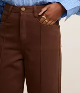 Pantalón wide leg de sarga color marrón chocolate, con cintura alta, trabillas, bolsillos delanteros y traseros, cierre con botón y cremallera, y costura vertical delantera.