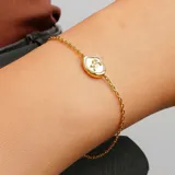 Pulsera dorada con cadena de eslabones finos y dije ovalado con borde dorado y centro blanco con el símbolo del signo zodiacal Capricornio en dorado.