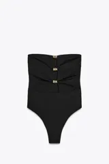 Bañador enterizo negro tipo bandeau, con escote recto, hombros descubiertos, copas extraíbles, forro interior y detalle de aberturas en el pecho con aplicación de anillas metálicas doradas.