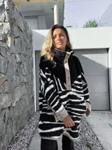 Buzo negro con estampado de cebra en blanco, con cuello alto y cierre parcial con botones a presión.