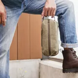 Neceser verde militar de tela canvas con detalles en cuero marrón. Tiene un bolsillo frontal con cierre, asa lateral y doble compartimento con cierre en la parte superior y en la base.