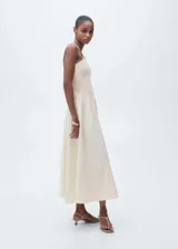 Vestido midi color crudo, con escote halter y tirantes finos. El corpiño es ajustado y texturizado, mientras que la falda es amplia y fluida.