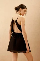 Vestido corto negro con escote en V, espalda descubierta y volados. Confeccionado en viscosa georgette, con breteles finitos que se atan en la espalda y ajuste elástico en la cintura.
