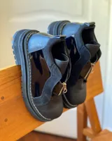 Botines de cuero negro con paneles laterales de charol, cierre frontal con cremallera y suela track.