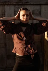 Camisa marrón con lunares blancos, corte clásico, cuello camisero, mangas 3/4 abullonadas y lazo ajustable en la cintura.