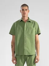 Camisa verde oliva de manga corta con textura waffle, corte cuadrado y bolsillo en el pecho. Cierre frontal con botones de coco grabados con el logo de la marca.