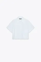 Camisa blanca corta con rayas verticales celestes, cuello solapa y mangas cortas con dobladillo. Tiene un bolsillo de parche en el pecho y cierre frontal con botones ocultos.