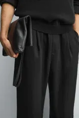 Pantalón negro de corte relajado con cintura elástica ajustable y pliegues en la parte delantera. Presenta bolsillos laterales y bolsillos traseros de parche.