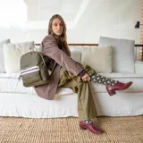 Mochila verde militar de nylon con detalles en símil cuero en el bolsillo frontal. Tiene asa de mano, correas regulables, bolsillo trasero vertical, dos bolsillos internos con cierre y un bolsillo abierto con división.