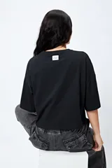 Remera blanca cropped de mangas cortas amplias con ojales metálicos a lo largo de las mangas.