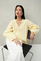 Blusa color amarillo pálido de manga larga con escote en V, mangas abullonadas con volados y botones forrados.