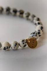 Pulsera elástica de piedras naturales color marrón con dije circular dorado con la palabra "AIRE" grabada.