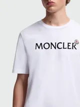 Camiseta blanca de manga corta con cuello redondo y el logo de Moncler estampado en negro en el pecho.