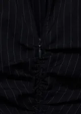Vestido corto camisero negro con finas rayas verticales blancas, cuello camisero, mangas largas con puños abotonados, cierre frontal con cremallera y frunces verticales en el centro.
