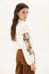 Camisa blanca de manga larga con bordados florales marrones en las mangas.