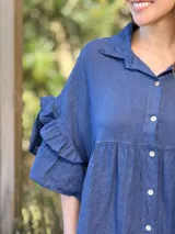 Vestido camisero azul de lino italiano, con cuello camisero, botones frontales, mangas 3/4 con doble volado y bolsillos laterales.