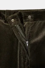 Pantalón de pana marrón oscuro, de tiro alto y corte ancho. Presenta bolsillos delanteros y trabillas en la cintura. Cierre frontal con cremallera y botón metálico.