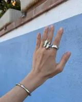 Anillo de diseño orgánico y macizo, realizado artesanalmente en bronce. Presenta una estructura abierta con dos piezas de forma irregular y textura rugosa.