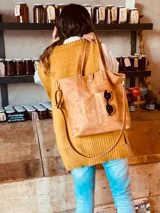 Bolso tipo tote bag color suela, de cuero, con doble asa de mano y correa larga extraíble y ajustable. Tiene dos bolsillos externos grandes.