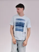 Remera celeste de manga corta con estampa rectangular con imagen del mar y texto en la parte superior.
