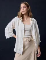 Camisa color crudo con bordado tipo broderie, cuello con solapa, manga tres cuartos y cierre frontal con botones.