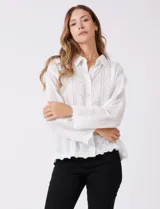 Camisa de algodón blanca con bordados florales verticales, cuello con solapa y cierre frontal con botones.