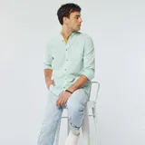 Camisa celeste claro de lino con cuello mao, manga larga con puños abotonados y bolsillo de parche en el pecho.