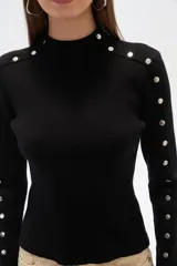 Sweater negro de punto con cuello alto y botones metálicos decorativos en hombros y mangas largas.