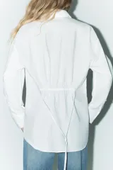 Camisa blanca de corte amplio, con cuello solapa, manga larga y cierre frontal con botones.
