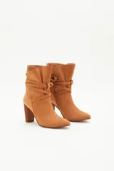 Botas de caña media de gamuza negra, con taco cuadrado y punta fina. Presenta tiras terminadas con borlas que se cruzan y atan alrededor de la caña.