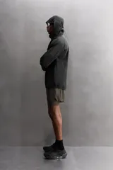 Cazadora negra de tejido técnico ripstop, con cuello alto, capucha ajustable y visera. Tiene mangas largas con puños elásticos, bolsillo de seguridad con cremallera en el pecho, bajo con elástico en los laterales y cierre frontal con cremallera.