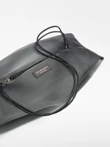 Bolso negro de malla con bolsa interior de piel y forro de algodón orgánico. Tiene cierre de cremallera lateral, asa corta fija y etiqueta exterior con logo.