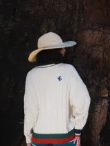 Buzo tejido verde con escote en V, cuello con rayas blancas y azul marino, y puños y ruedo con detalle de rayas.