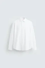 Camisa blanca de corte regular fit, cuello italiano, manga larga con puños abotonados y cierre frontal con botones.