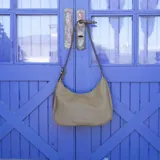 Cartera negra ovalada de simil cuero con cierre y correa ajustable con ojales. Cuenta con bolsillos internos y un bolsillo trasero.