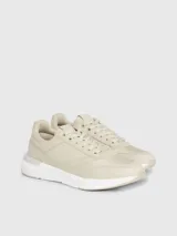 Zapatillas urbanas color beige, confeccionadas en cuero y tela, con suela blanca y cordones. Presentan monograma de la marca en el lateral.