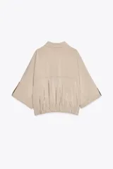 Camisa color beige de cuello solapa y manga corta con trabilla y botón. Tiene bolsillos delanteros de plastrón con solapa, bajo con elástico y cierre frontal con botones a presión.