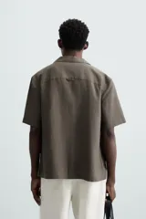 Camisa color marrón oscuro de corte relaxed fit, confeccionada en tejido de lino. Tiene cuello bowling, manga corta, bajo con aberturas laterales y cierre frontal de botonadura.
