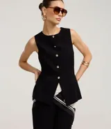 Chaleco negro de sastrería con cuello redondo, cierre frontal con botones dorados y bajo estructurado con recortes anatómicos.