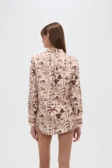 Camisa de manga larga con estampado de motivos playeros en tonos marrones sobre fondo beige, cuello camisero y cierre frontal con botones.