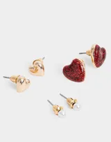 Set de tres pares de aros pasantes: un par de perlas, un par de corazones dorados y un par de corazones rojos con glitter.