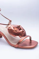 Sandalias de cuero color champagne, con taco cuadrado, tira delgada sobre los dedos y tobilleras para atar. Presentan un aplique de flor de cuero en la capellada.