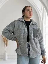 Campera gris de tela tipo peluche con cierre frontal y bolsillo de cuero sintético en el pecho.
