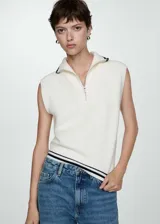 Chaleco de punto color crema, con cuello polo con cierre de cremallera, sin mangas y terminaciones en punto canalé.