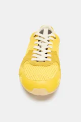 Zapatillas deportivas amarillas con detalles en negro y blanco. Presentan una combinación de materiales y texturas en el cuerpo, tirador en la lengüeta y cierre mediante cordones.