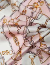 Pañuelo cuadrado de satén con estampado de cadenas doradas y detalles en rosa y blanco.