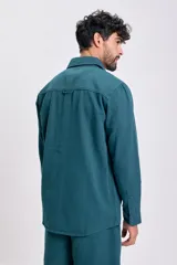 Camisa de manga larga color verde azulado, con cuello camisero, botones frontales y dos bolsillos de parche con tapa en el pecho.